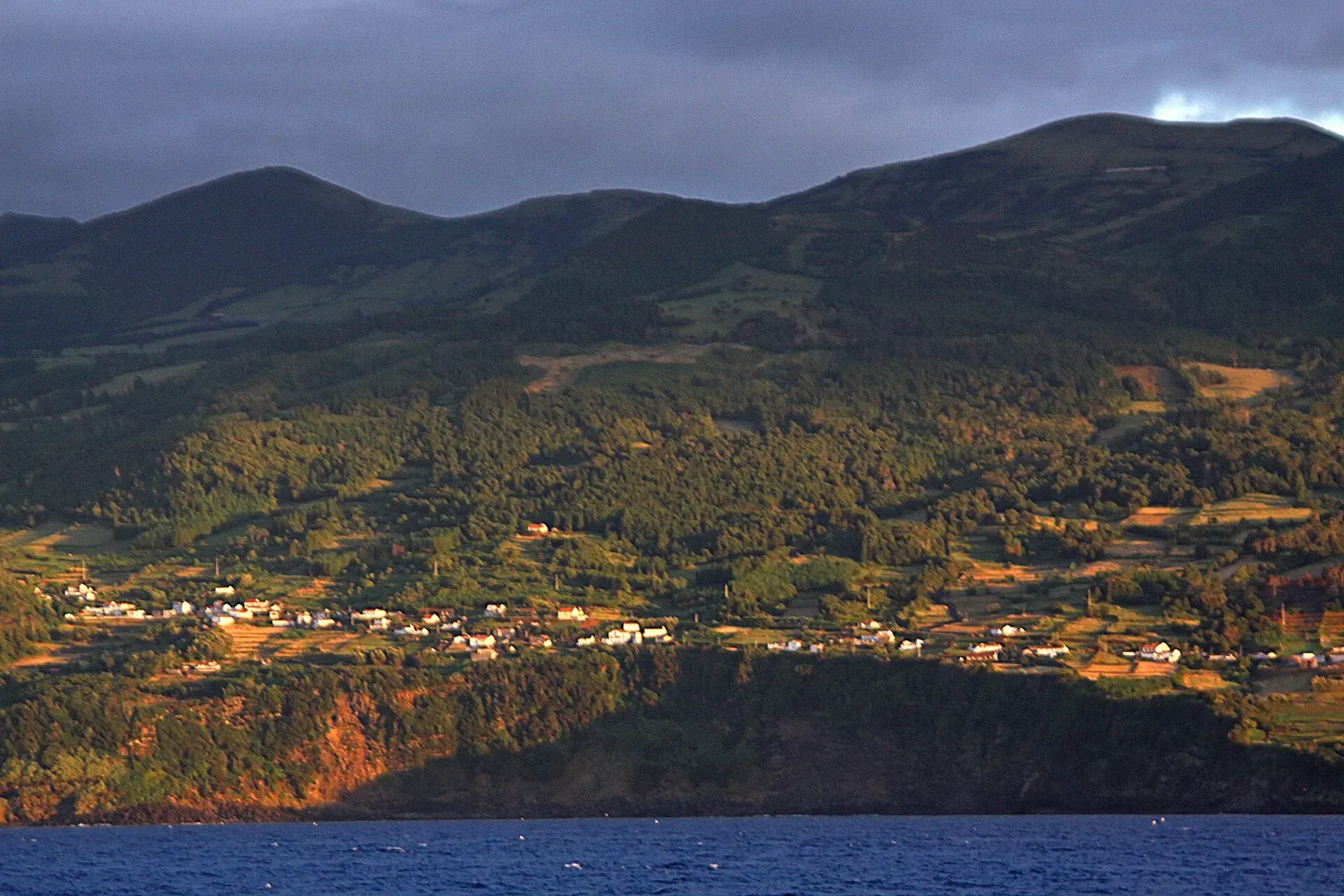 Costa y casas de São Roque do Pico vistas desde el mar, con las laderas de la isla al fondo